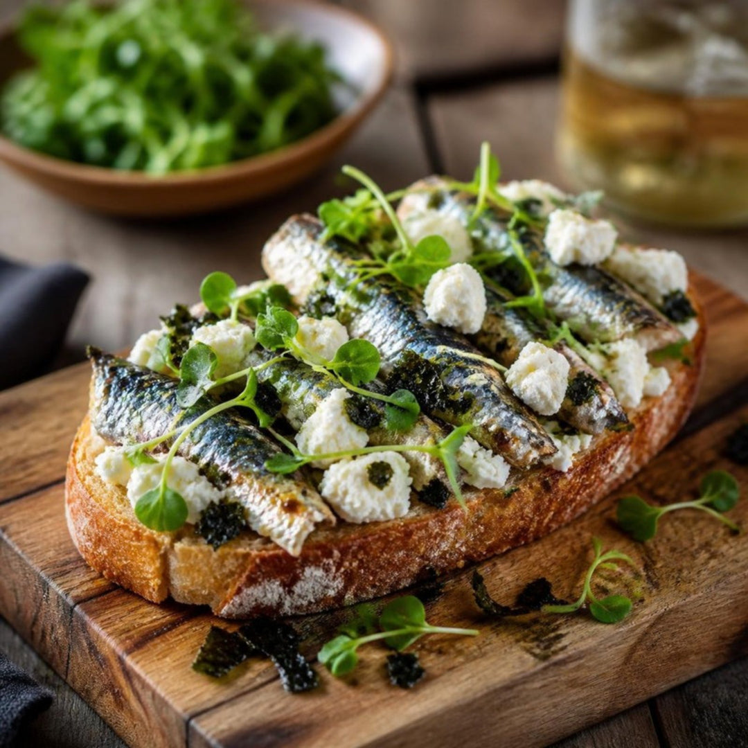 Sardine toast on a wooden board: whole sardine fillets on crusty toast with crumbled feta, seaweed flakes and microgreens