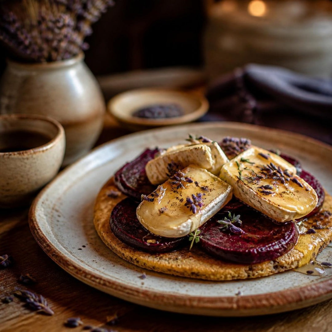 A golden socca pancake topped with slices of beetroot and camembert, sprinkled with dried lavender and drizzled with honey