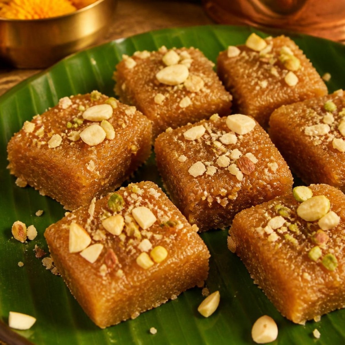 Squares of coconut jaggery barfi topped with chopped nuts on a banana leaf
