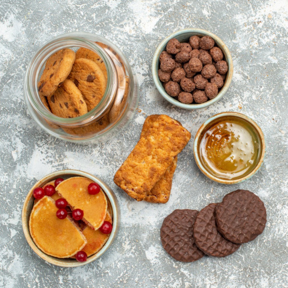 Organic biscuits, chocolate bites, honey, tart and bar on grey concrete